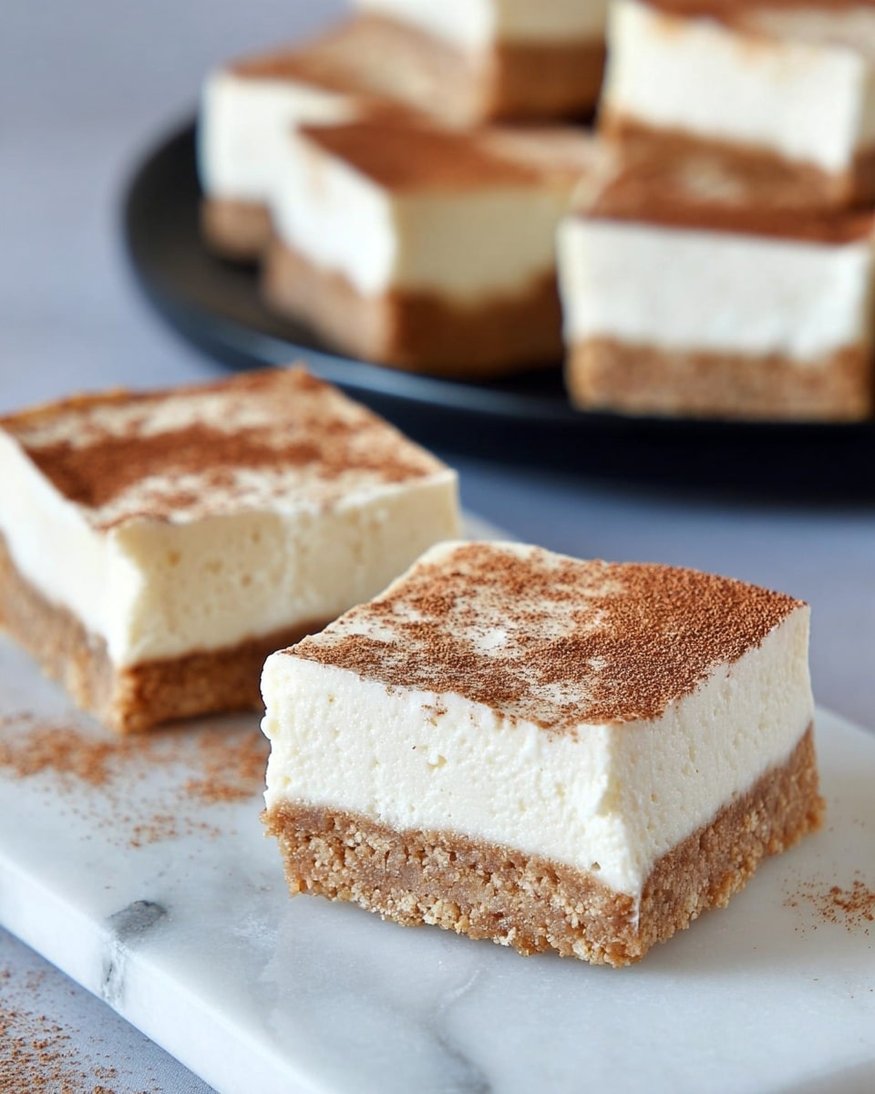 The image shows slices of a three-layer dessert bar on a white marbled surface. The bottom layer is a thick, crumbly light brown crust with visible texture. Above it is a thick, smooth, creamy white middle layer that looks soft and rich. The top layer is a thin dusting of cinnamon or spice, giving a light brown, slightly speckled look with some granules of sugar visible. The dessert slices are rectangular, and in the background several more pieces are arranged on a black plate. The colors mainly include white, light brown, and cream, all against the white marbled surface. Photo taken with an iphone --ar 4:5 --v 7