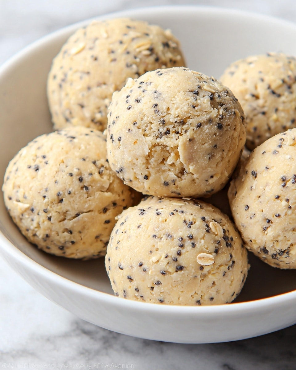 The image shows a close-up of several round, beige balls with a rough texture, placed inside a white bowl. Each ball is speckled with small black seeds and bits of oats embedded in the dough, giving them a speckled and slightly uneven look. The balls have a soft, crumbly surface with some small cracks and oats visible on top. The bowl sits on a white marbled surface, and the photo captures the texture and details of the balls clearly. photo taken with an iphone --ar 4:5 --v 7