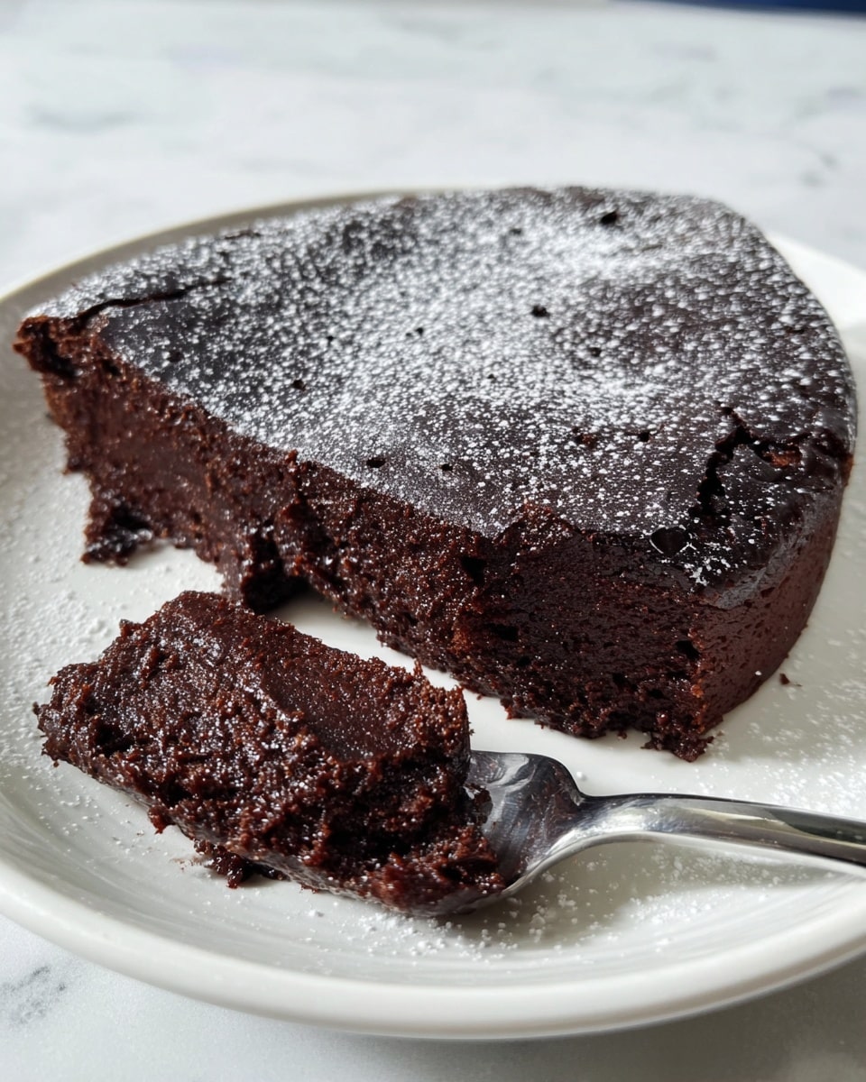 A moist, dark chocolate brownie with a slightly glossy, cracked top layer sits on a round white plate with light dusting of powdered sugar. The brownie itself is thick, almost fluffy on the inside with visible air bubbles creating a soft texture. A piece has been cut and is shown on a silver fork resting near the front of the plate, revealing the dense, rich interior beneath the baked crust. The scene is set against a white marbled textured surface, giving a clean and bright look. photo taken with an iphone --ar 4:5 --v 7