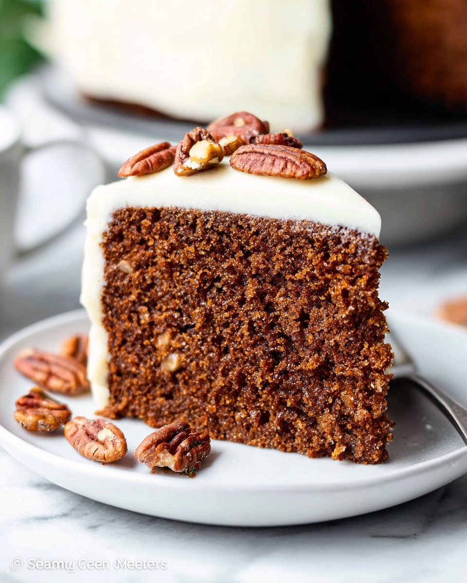 A single slice of moist, dark brown cake with a dense, textured crumb sits centered on a white plate. The cake has one visible layer topped with a thick, smooth, creamy white frosting. Scattered on top of the frosting are several whole and halved pecans, adding a crunchy contrast. Some pecan pieces also lie on the plate near the cake. The background is a soft focus with a white marbled texture surface partly visible beneath the plate. photo taken with an iphone --ar 4:5 --v 7