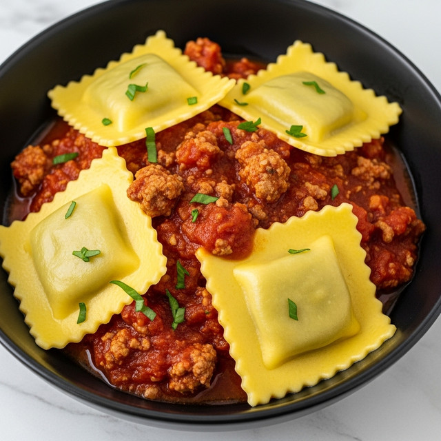 This image shows a close-up of a black bowl filled with a rich tomato sauce mixed with ground meat. On top, there are four golden yellow ravioli pieces with ruffled edges, each slightly glossy from sauce and garnished with small green herbs. The thick sauce is chunky with bits of meat and tomato evenly spread around the ravioli, giving a hearty and textured look. The black bowl contrasts well with the warm colors of the food, and the background is a white marbled texture. photo taken with an iphone --ar 4:5 --v 7