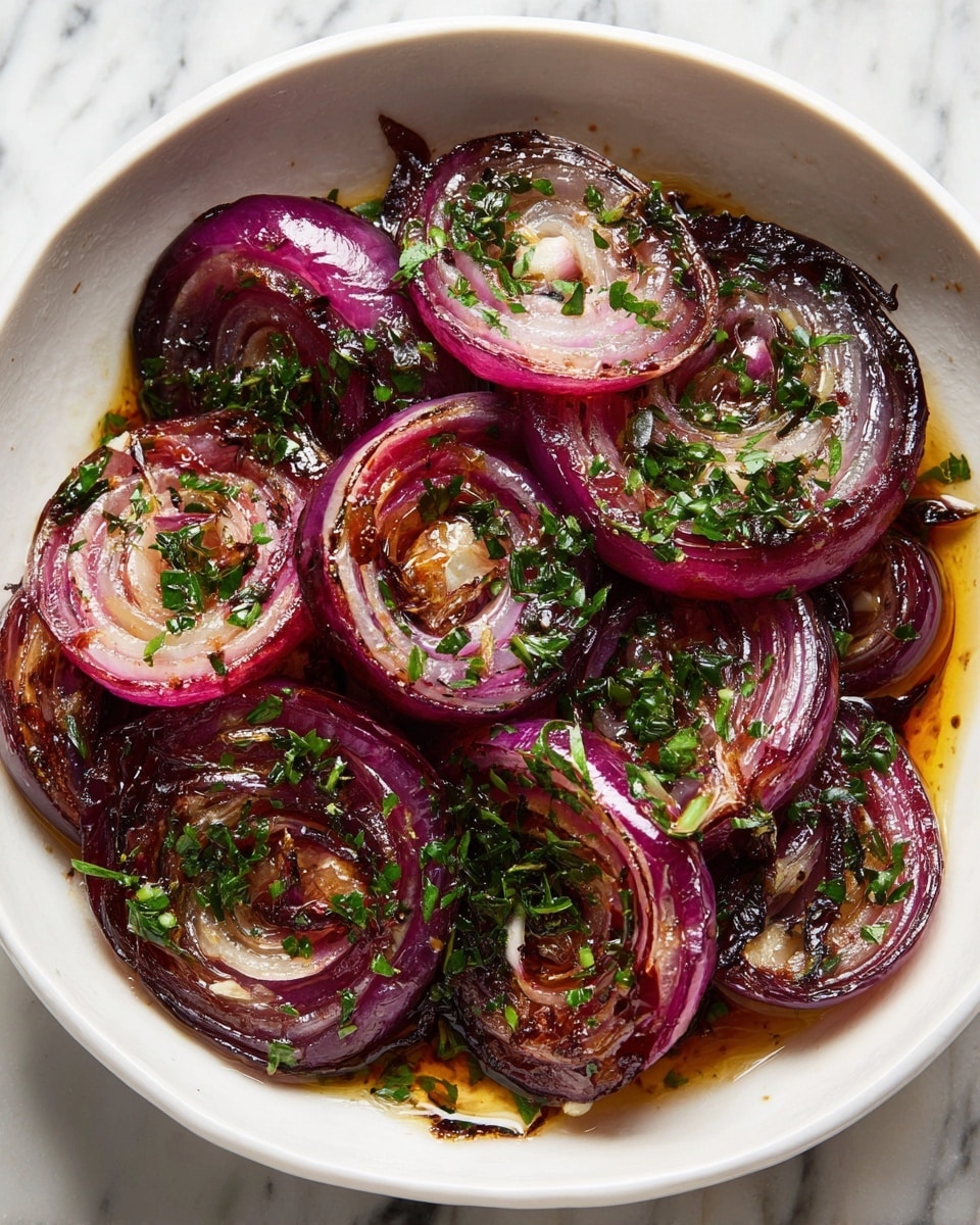 The image shows a white square bowl filled with thick slices of cooked red onion, each slice slightly separated into rings. The onions have a glossy, caramelized surface with a mix of golden brown and deep pink tones, showing a soft texture with some crispy, charred edges. Finely chopped green herbs are sprinkled generously over the onions, adding pops of fresh green color that contrast with the rich, dark caramelization. There is a light coating of oil pooling at the bottom of the bowl, enhancing the shiny look of the dish. The bowl is set on a white marbled surface. photo taken with an iphone --ar 4:5 --v 7