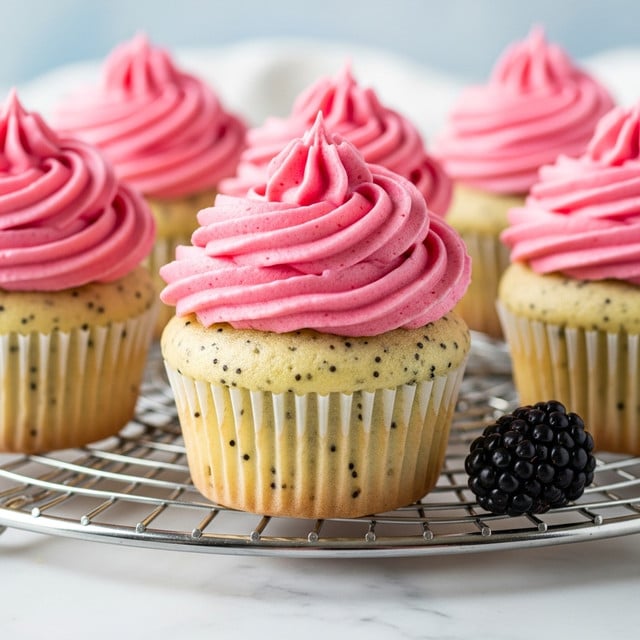 A close-up of five vanilla cupcakes with small black specks baked into light yellow cake bases, each topped with a thick swirl of bright pink frosting. The frosting has a smooth, creamy texture with soft peaks and is piped high on each cupcake. The cupcakes sit on a silver cooling rack placed over a white marbled surface, with a single blackberry resting near the edge of the rack. The background is softly blurred with light blue and white hues, keeping focus on the cupcakes. photo taken with an iphone --ar 4:5 --v 7