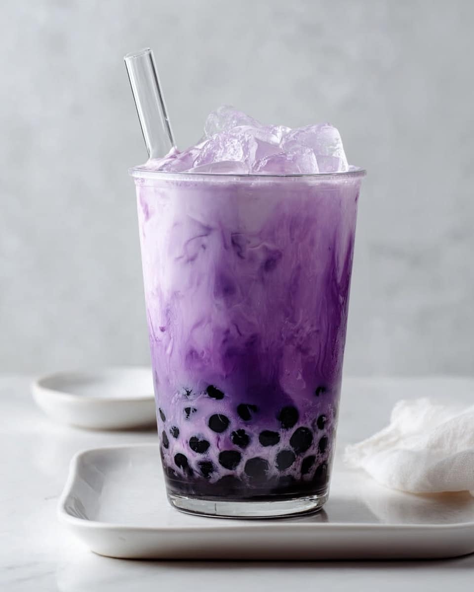 The image shows a clear glass filled with a layered purple drink. At the bottom, there are black tapioca pearls that are round and shiny. Above the pearls, the drink has a gradient effect, starting with a deep purple at the bottom that blends smoothly into a lighter purple color near the top. Some white ice cubes float inside the glass, visible through the drink. A white straw is placed in the middle, sticking out of the glass. The glass sits on a white tray with a small white bowl beside it, all set on a white marbled surface. Photo taken with an iphone --ar 4:5 --v 7