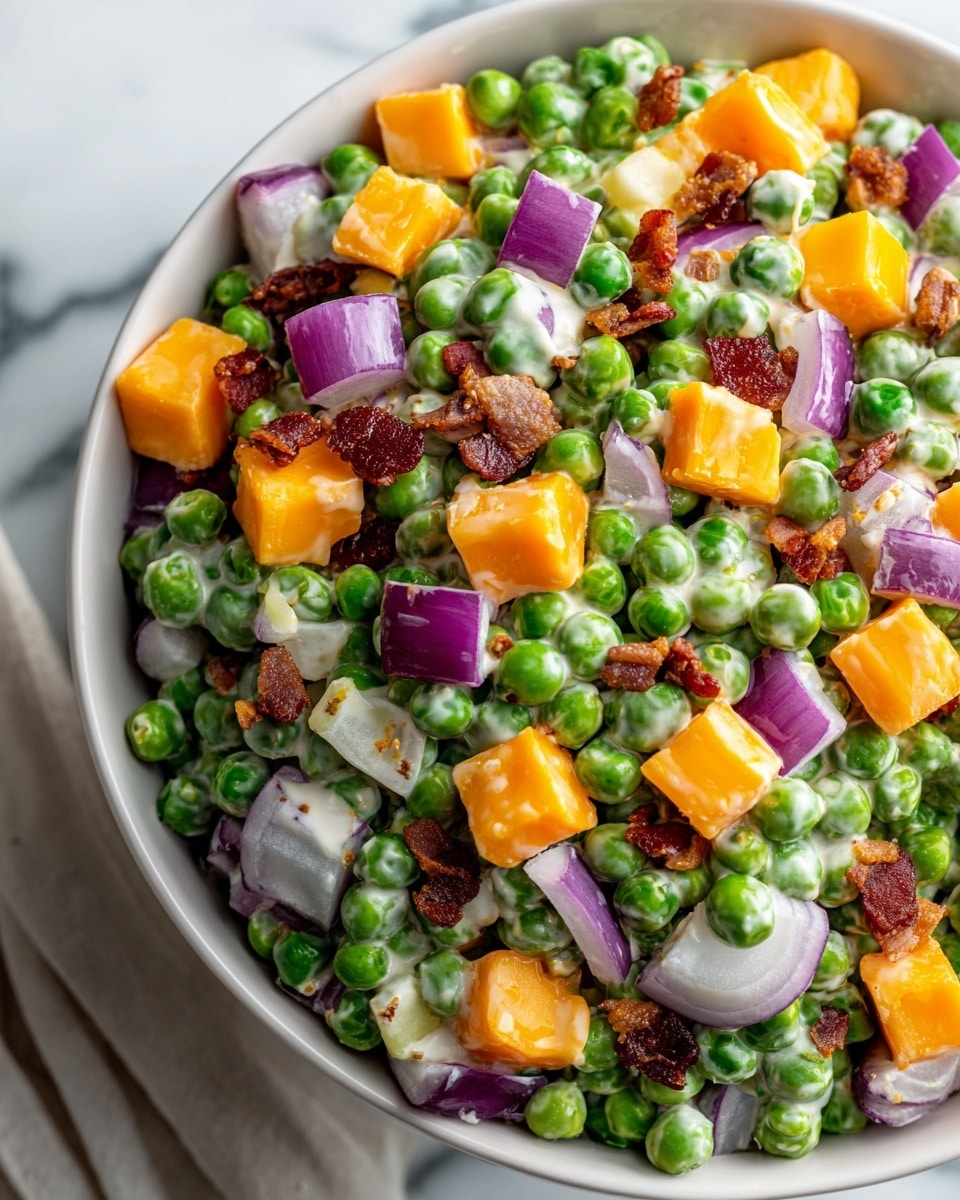 A close-up view of a creamy salad in a white bowl on a white marbled surface, showing three main layers mixed together: bright green peas, large yellow-orange cheese cubes, and small chopped red onion pieces with creamy dressing evenly coating all ingredients. There are also small bits of crispy bacon scattered throughout, adding texture and a reddish-brown color contrast. Red onion rings are placed around the bowl on the white marbled surface, enhancing the scene's freshness. photo taken with an iphone --ar 4:5 --v 7