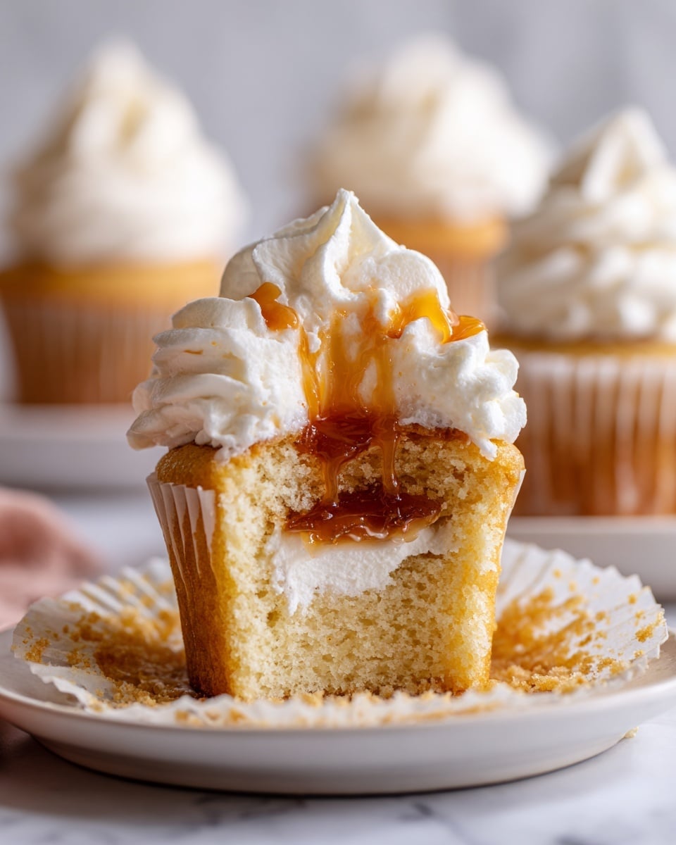 A close-up of a vanilla cupcake with three visible layers: the base layer is a light golden, soft, and crumbly cake; the middle layer is a thick white cream filling with a glossy, amber-colored jelly center; and the top layer is a generous swirl of smooth white frosting with soft peaks. The cupcake sits on a white plate with a white marbled background, and blurred similar cupcakes are visible in the background. photo taken with an iphone --ar 4:5 --v 7