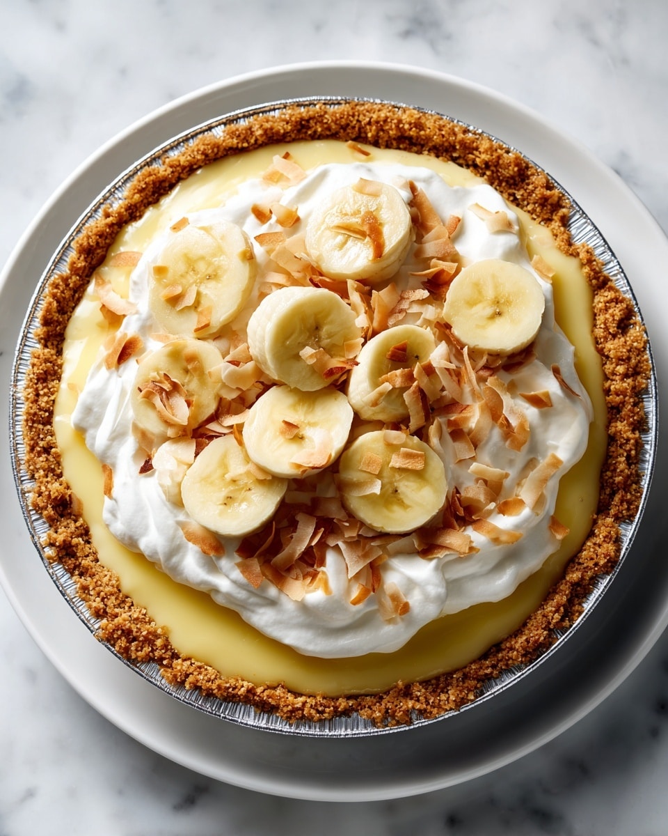 A close-up of a pie showing four layers, placed on a white plate over a white marbled surface. The bottom layer is a crumbly, brown crust in a silver foil pie pan. On top of the crust is a smooth, pale yellow creamy custard layer. The third layer consists of evenly arranged banana slices covering the custard. The top layer is thick, white whipped cream piped in fluffy swirls, decorated with more banana slices standing on edge and a sprinkling of small, toasted coconut flakes in the center. photo taken with an iphone --ar 4:5 --v 7