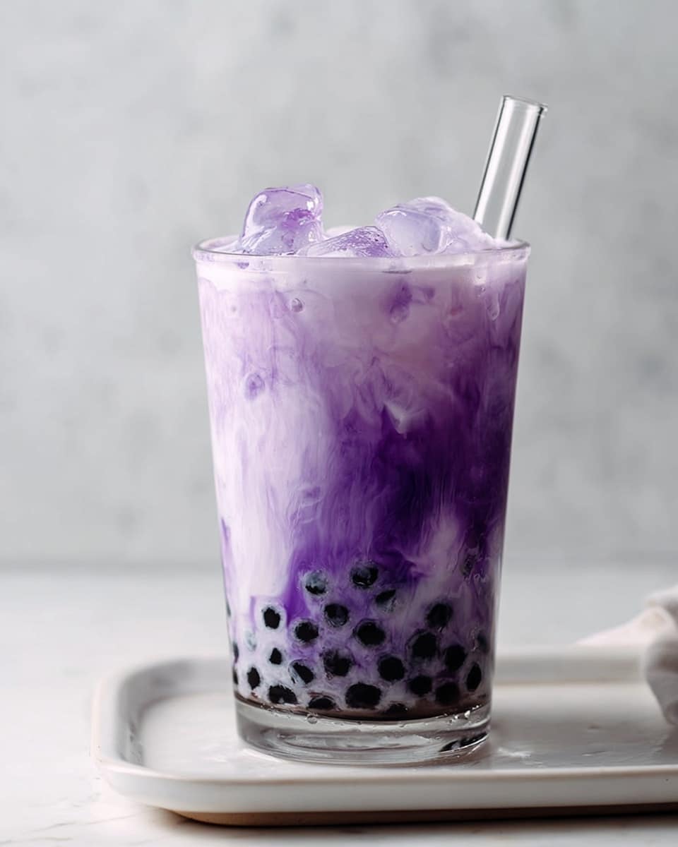 A clear cup filled with a layered purple drink, starting from the bottom with black tapioca pearls, followed by a cloudy mix of light and dark purple swirls, topped with a frothy, thicker purple layer with ice cubes visible inside. A transparent straw is placed in the cup, and it sits on a white tray against a white marbled background. photo taken with an iphone --ar 4:5 --v 7