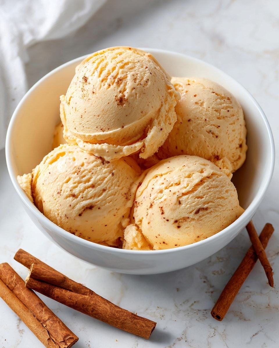 A white bowl holds four scoops of creamy orange ice cream with visible specks that show its spiced flavor. The scoops are smooth with a slightly melting texture, fitting snugly together in the bowl. Around the bowl, there is a white marbled surface with cinnamon sticks, adding a warm aroma feel to the photo. The bright lighting highlights the ice cream’s rich color and creamy texture. Photo taken with an iphone --ar 4:5 --v 7