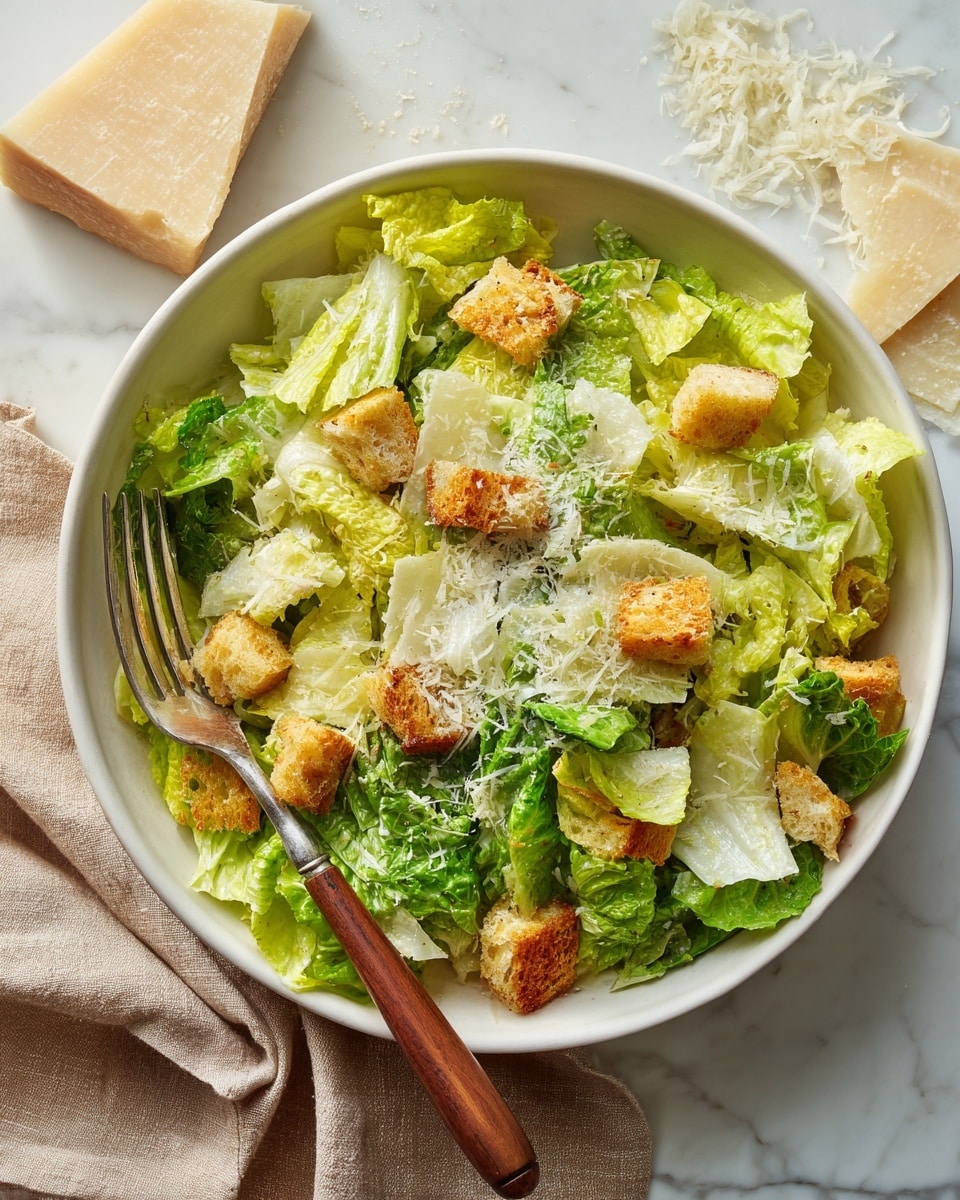 The image shows a white bowl filled with a fresh Caesar salad placed on a white marbled surface. The salad has a base layer of crisp, green romaine lettuce with varying shades of light to medium green. Scattered on top are crunchy, golden-brown croutons. The salad is sprinkled with a generous amount of finely grated pale yellow Parmesan cheese shavings, giving it a light, fluffy texture. A fork with a wooden handle rests inside the bowl on the left side. In the background, there is a small block of Parmesan cheese with some shavings around it. The setting features a beige cloth under the bowl and the overall scene has bright, natural lighting that highlights the freshness of the ingredients. photo taken with an iphone --ar 4:5 --v 7