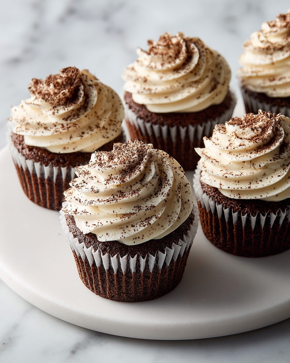Five cupcakes sit closely together on a round white marble surface. Each cupcake has one bottom layer of moist, light brown cake wrapped in a white liner. On top, a thick swirl of creamy, off-white frosting rises in three visible layers, with a soft and smooth texture. The frosting is evenly dusted with fine dark brown cocoa powder, giving a speckled effect. The cupcakes are photographed in soft natural light, highlighting their fluffy and rich texture. Photo taken with an iphone --ar 4:5 --v 7