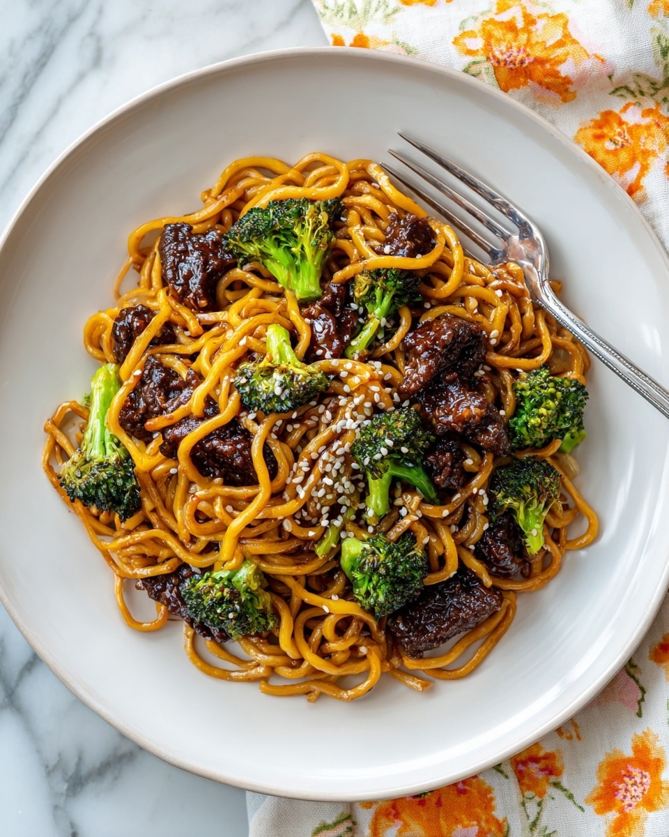 The dish shows a white plate filled with a mix of bright golden-brown noodles and dark brown glazed beef pieces scattered throughout, with small green broccoli florets adding freshness in between. The noodles are twisted in multiple loops and layered thickly, their smooth shine from sauce catching light. The beef chunks have a slightly charred, glossy texture, contrasting well with the green broccoli, which looks steamed and tender. On top, white sesame seeds are sprinkled evenly, adding small spots of light contrast. A silver fork rests on the right side of the plate, partially tucked under the noodles. The plate sits on a white marbled surface with part of another similar plate and a floral cloth with orange flowers partly in the frame. Photo taken with an iphone --ar 4:5 --v 7
