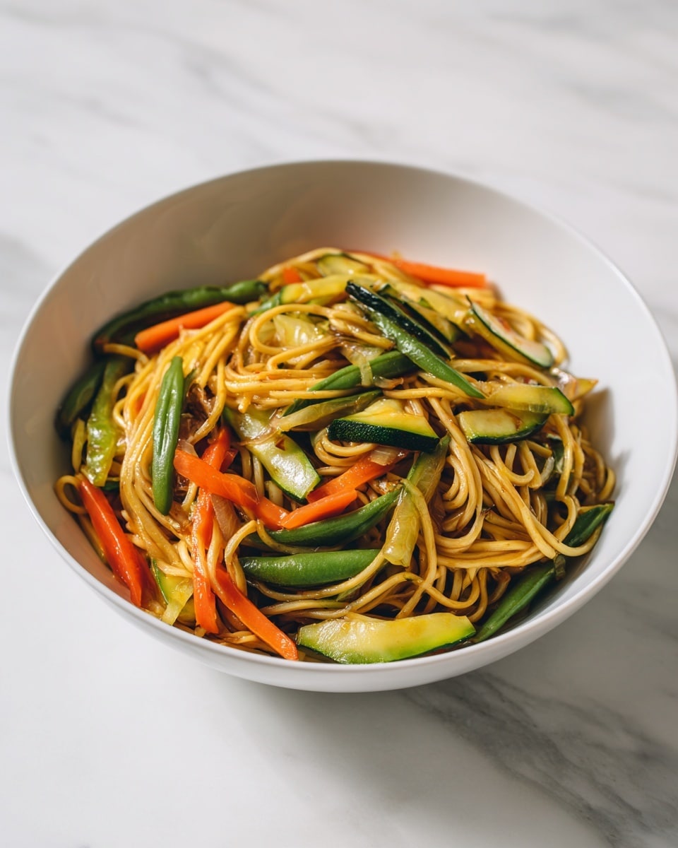 A white bowl full of stir-fried noodles with a mix of sliced vegetables, including green zucchini, orange carrots, and green beans. The noodles are golden brown and slightly shiny, twisted and piled loosely in the bowl. The vegetables are mixed evenly throughout the noodles, adding color contrast and fresh texture. The bowl sits on a white marbled surface, with natural light brightening the scene. Photo taken with an iphone --ar 4:5 --v 7