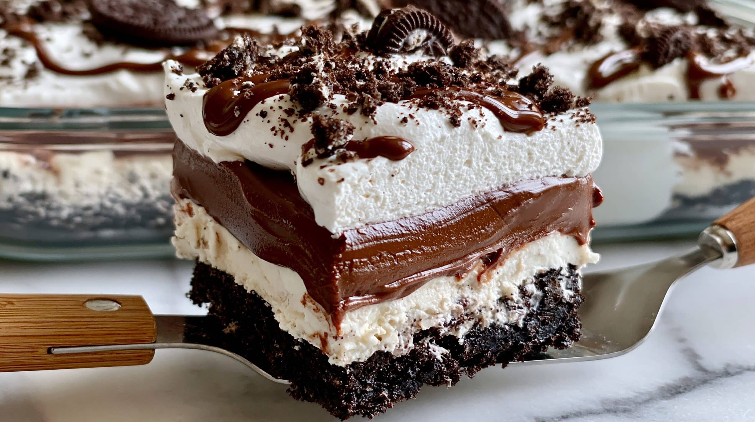 A close-up of a square slice of a layered Oreo dessert being lifted with a metal spatula that has a wooden handle, showing four visible layers: at the bottom a dark and crumbly Oreo crust, above it a thick white creamy layer, then a rich and glossy chocolate layer with some dripping down the edge, and on the top a fluffy white whipped cream layer sprinkled with broken Oreo pieces and a drizzle of chocolate. The dessert is in a clear glass baking dish placed on a white marbled surface. The background shows the rest of the dessert in the baking dish with more Oreo crumbs and chocolate drizzle on top. photo taken with an iphone --ar 4:5 --v 7