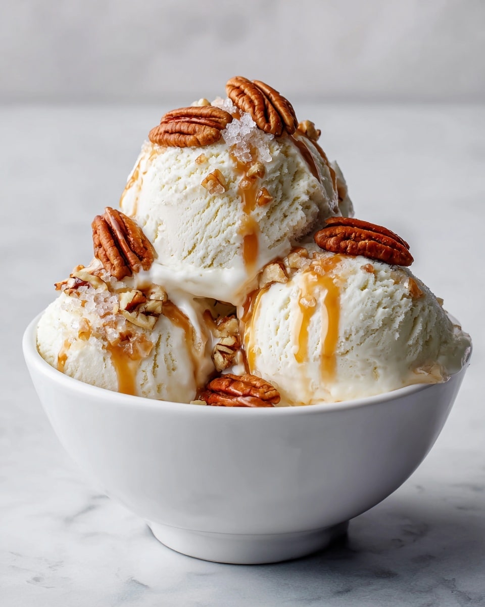 The image shows three scoops of creamy white ice cream in a white bowl on a white marbled surface. Each scoop has a rough texture with visible ice crystals on top. A thick caramel sauce is drizzled over the ice cream, creating smooth, shiny amber streaks. On top of the scoops, there are whole pecans and coarse grains of salt that add texture and detail. The scene is close up, highlighting the contrast between the creamy ice cream, glossy caramel, and crunchy pecans, with soft natural lighting. Photo taken with an iphone --ar 4:5 --v 7