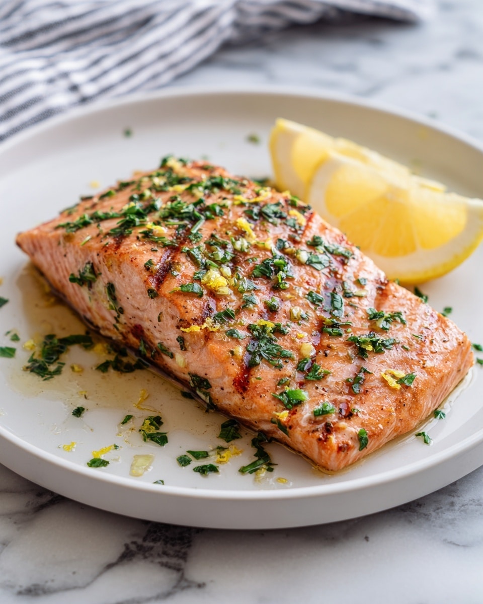A thick piece of grilled salmon with a golden brown color and charred grill marks sits centered on a clean white plate. The salmon is topped with small bits of green herbs and tiny yellow zest pieces that add bright contrast. To the side of the fish are two fresh lemon wedges with a vibrant yellow color. Scattered around the plate are some extra bits of chopped herbs and zest. The plate rests on a white marbled surface with a gray striped cloth napkin folded softly nearby. Photo taken with an iphone --ar 4:5 --v 7