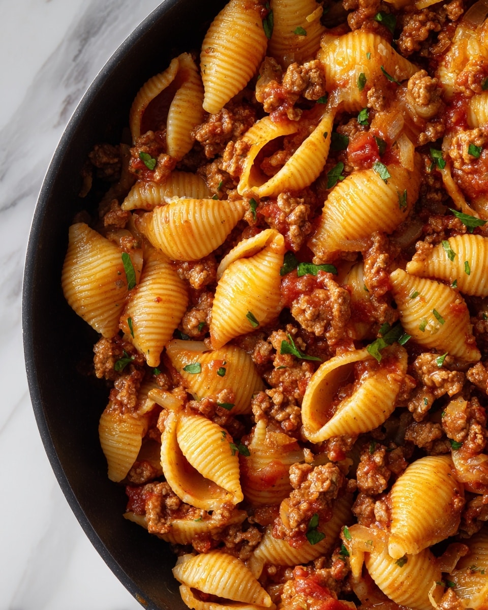 A close-up view of shell-shaped pasta mixed with a thick meat sauce in a black pan. The pasta is a pale yellow color with ridges, coated in a rich red tomato sauce filled with small, browned ground meat pieces and diced onions and tomatoes. Green chopped parsley is sprinkled evenly on top, adding a fresh touch of color. The sauce looks thick and glossy, filling the pasta shells and clinging to the meat. The overall texture is hearty and chunky, with the varied shapes and colors of the ingredients blending well. Photo taken with an iphone --ar 4:5 --v 7
