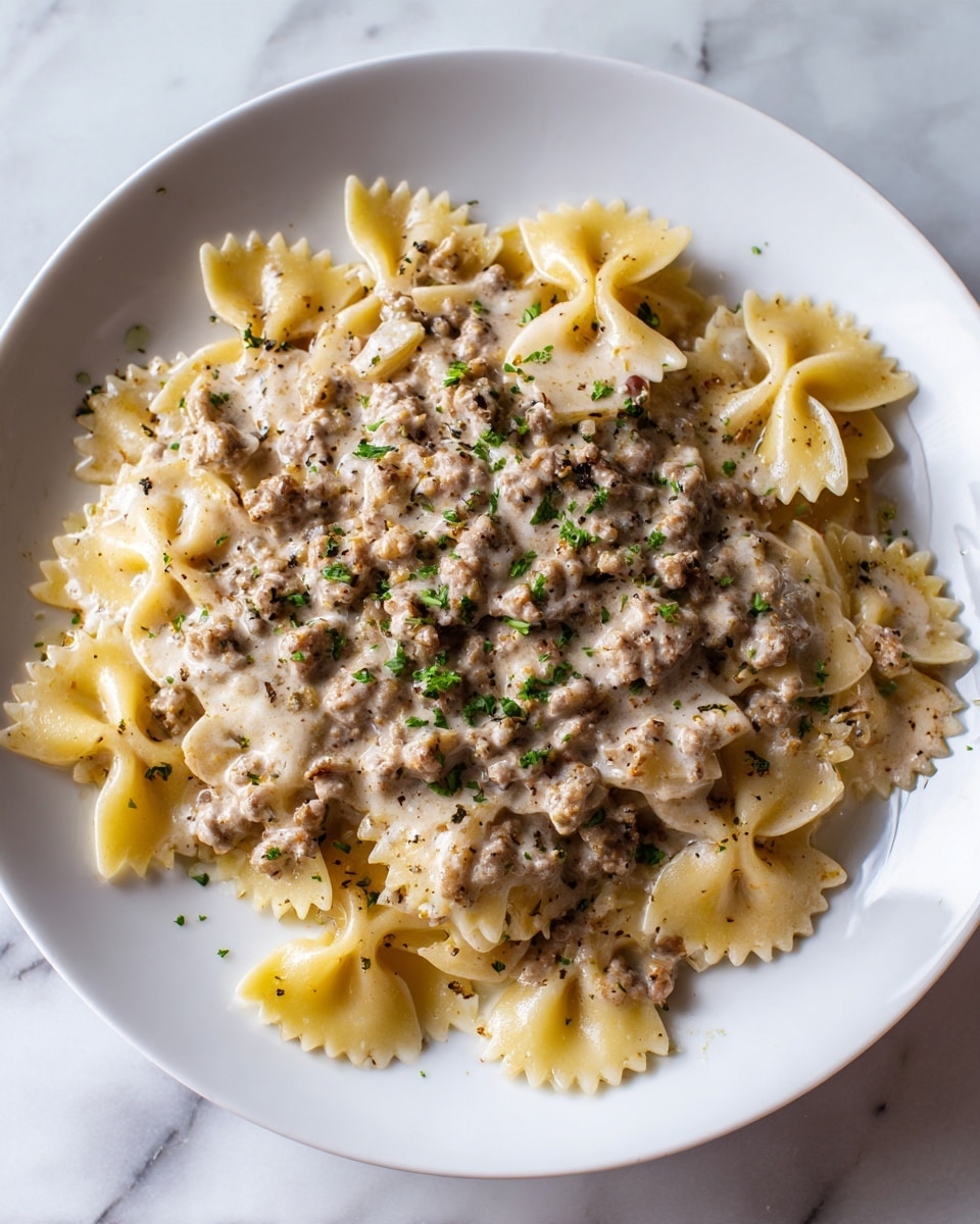 A white round plate filled with farfalle pasta mixed with a thick creamy sauce and cooked minced meat spread evenly over the top. The pasta is golden yellow with a smooth texture, while the meat sauce is light brown and chunky. There are small green herb leaves sprinkled on top for color contrast. The dish is placed on a white marbled surface. Photo taken with an iphone --ar 4:5 --v 7